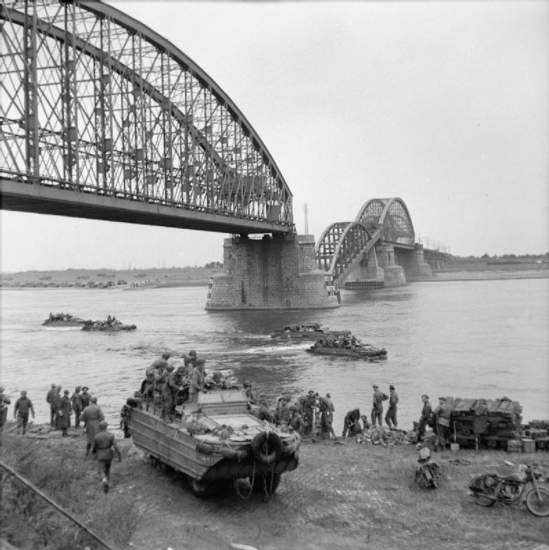 DUKWs from the British Army transport supplies across the River Waal at Nijmegen, below the railway bridge whose central span was broken by German frogmen using floating mines