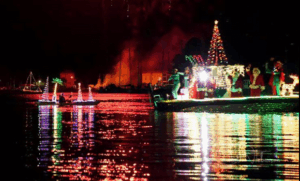 Lighted boat sits in the harbor with a red firework bursting above
