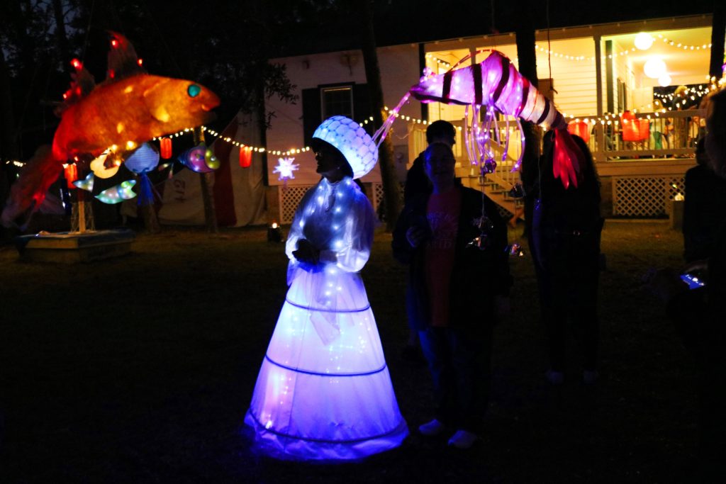 Lady in glowing costume surrounded by colorful hanging lanterns
