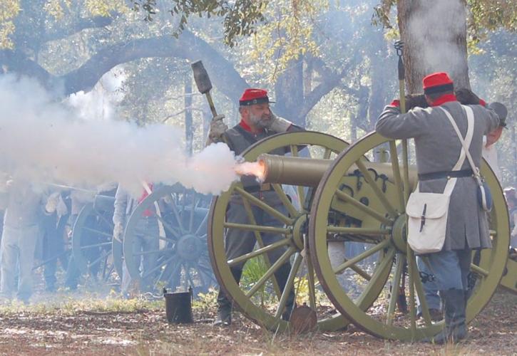 Cannon is fired by two men in confederate gray uniforms
