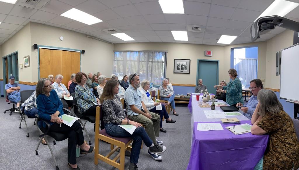 Group of attendees sit and listen to 5 speakers behind a panel table