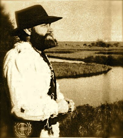 Man standing in profile looking right with a river and marsh behind him.