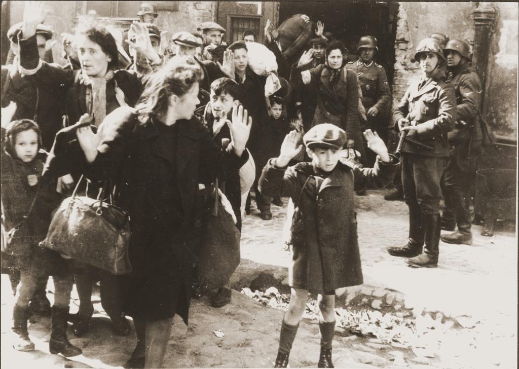Photo showing a small boy holding his hands up while a WWII Nazi soldiers points a gun at him