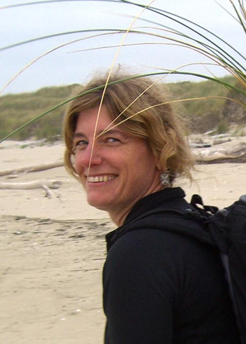 Lady walks along the shoreline with dune grasses in her backpack