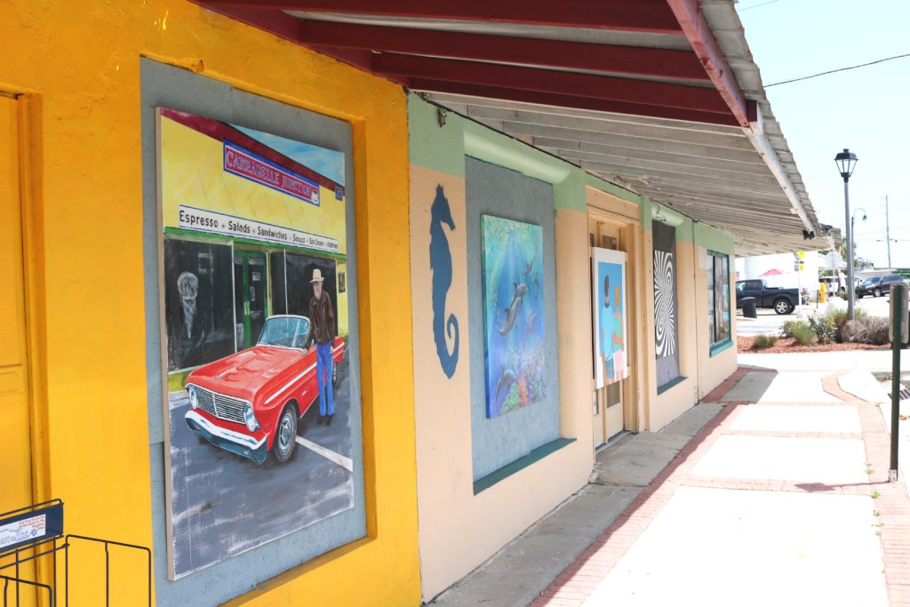 Several large paintings hang on the outside of the windows of an empty storefront