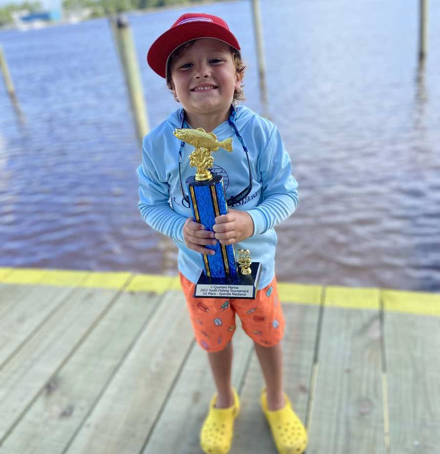Child standing on a wooden dock with water behind him holds a trophy