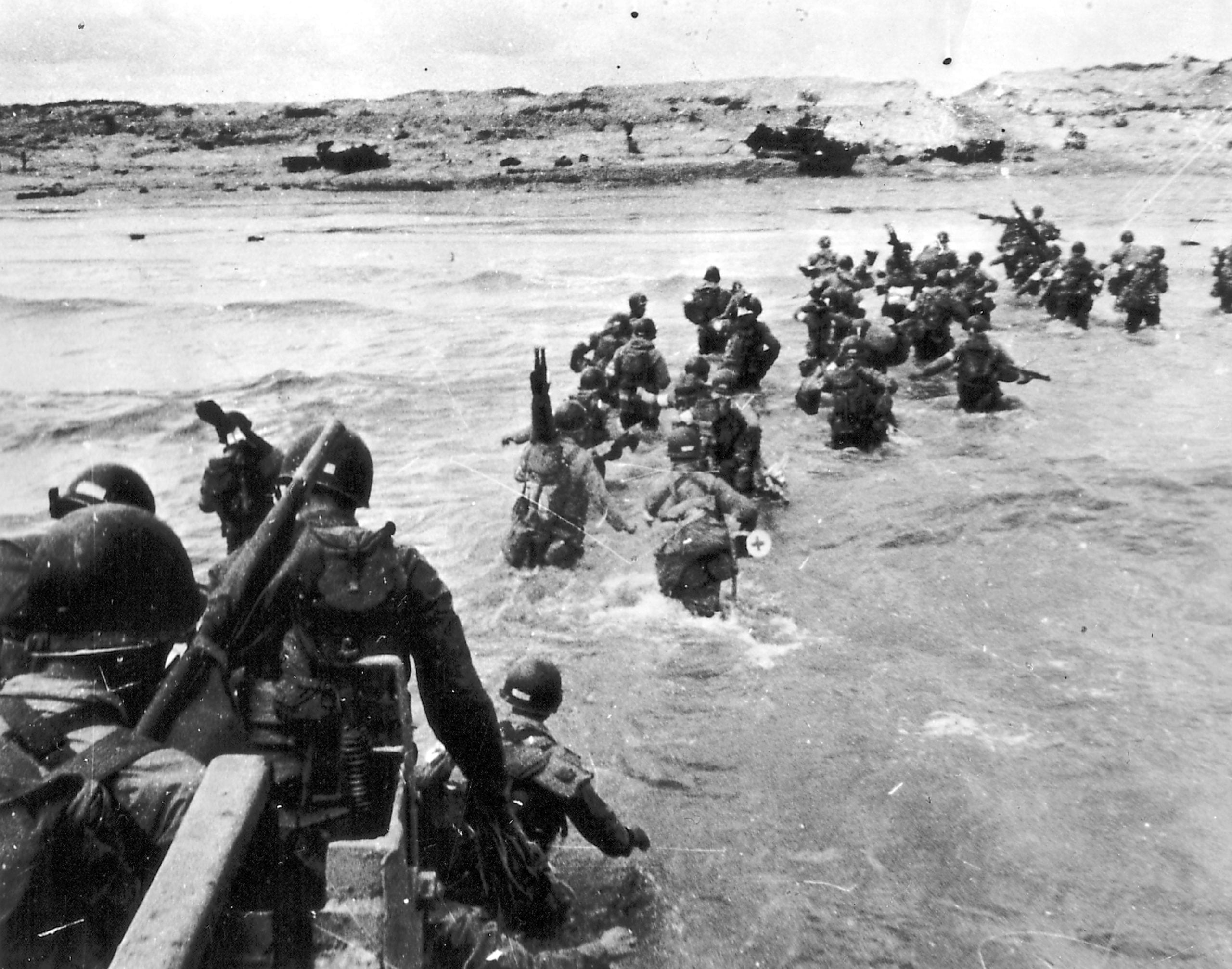 WWII soldiers wade through waist deep ocean water towards a shortline