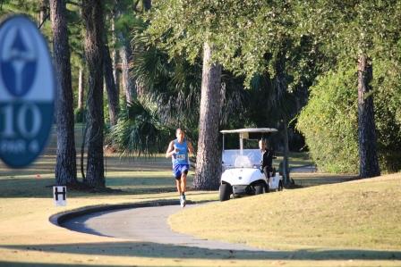 Man jogs along a path with a golf cart following behind