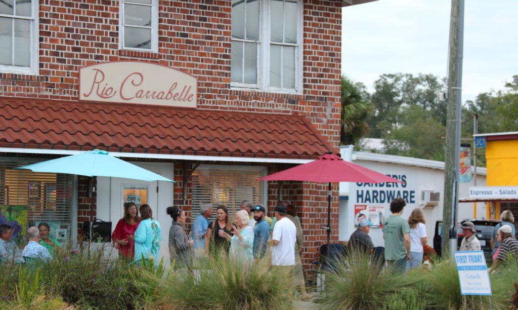 People gather and talk on the outdoor patio of a two story red brick building.