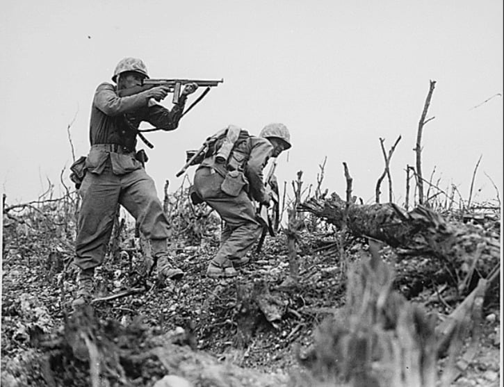A WWII Marine points a gun as his companion ducks for cover near Shuri. Okinawa, 1945.
