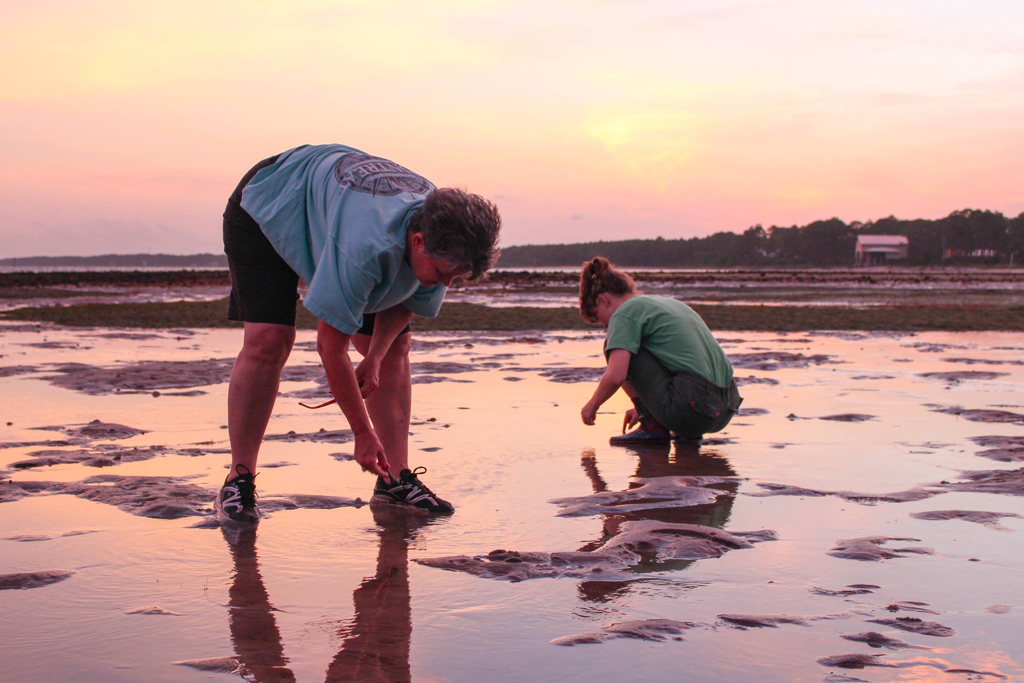 Two people bend down to examine things along the ocean shore